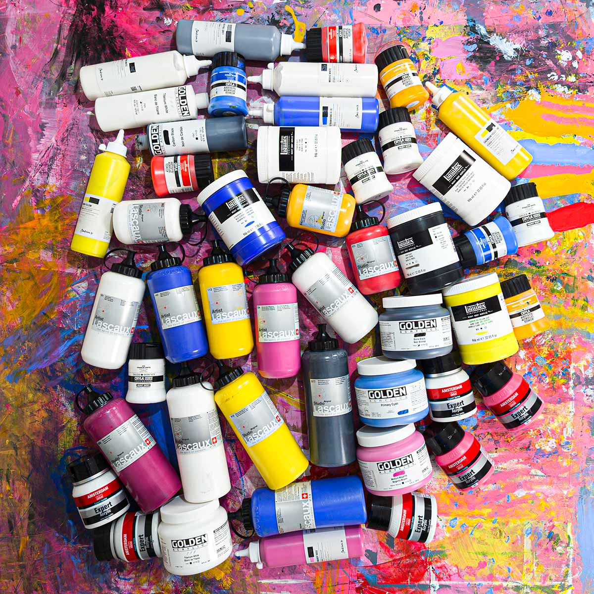Assorted acrylic paint tubes and jars on a colourful paint-covered workbench