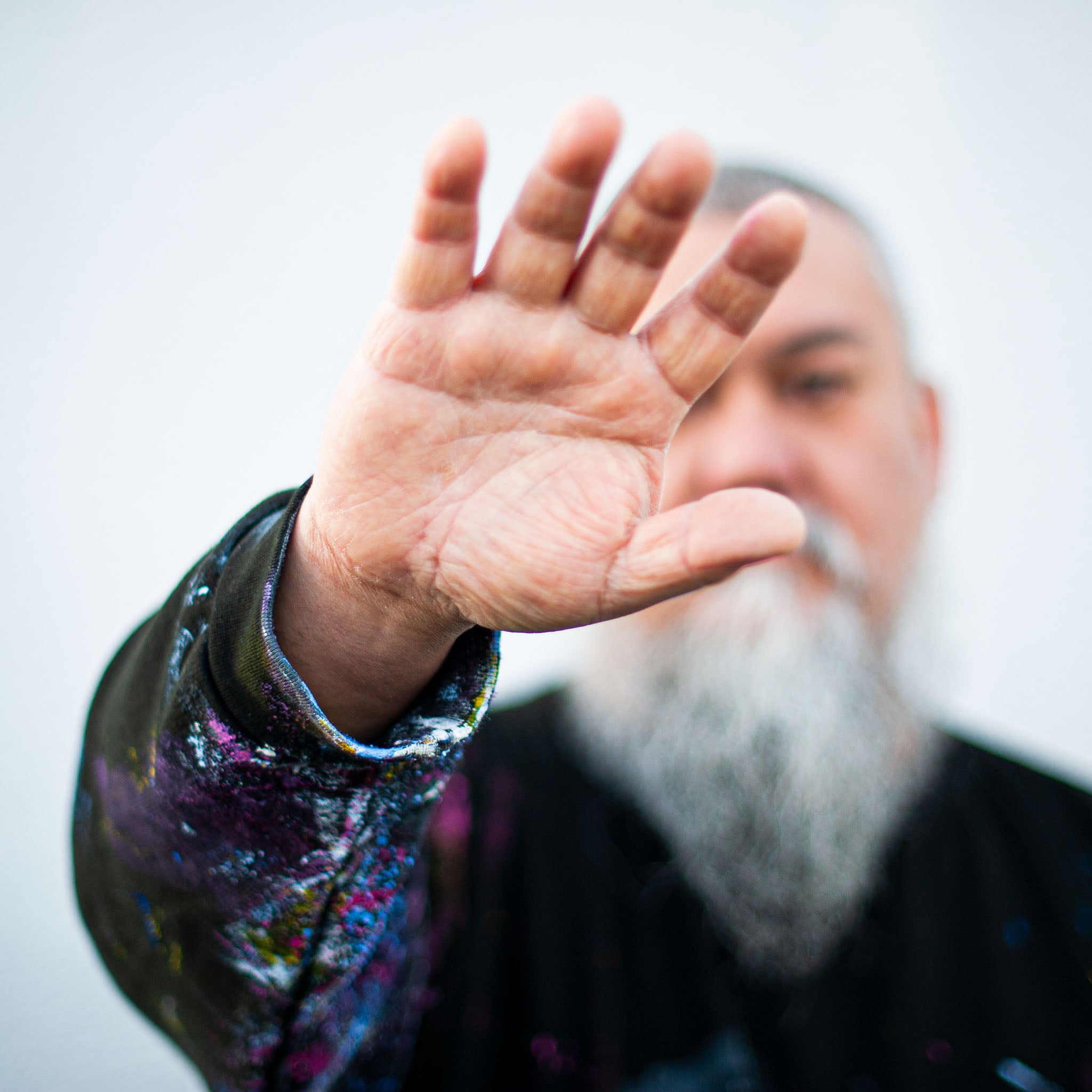 Artist raising a paint-covered hand, wearing a paint-splattered jacket, symbolising the creative process.