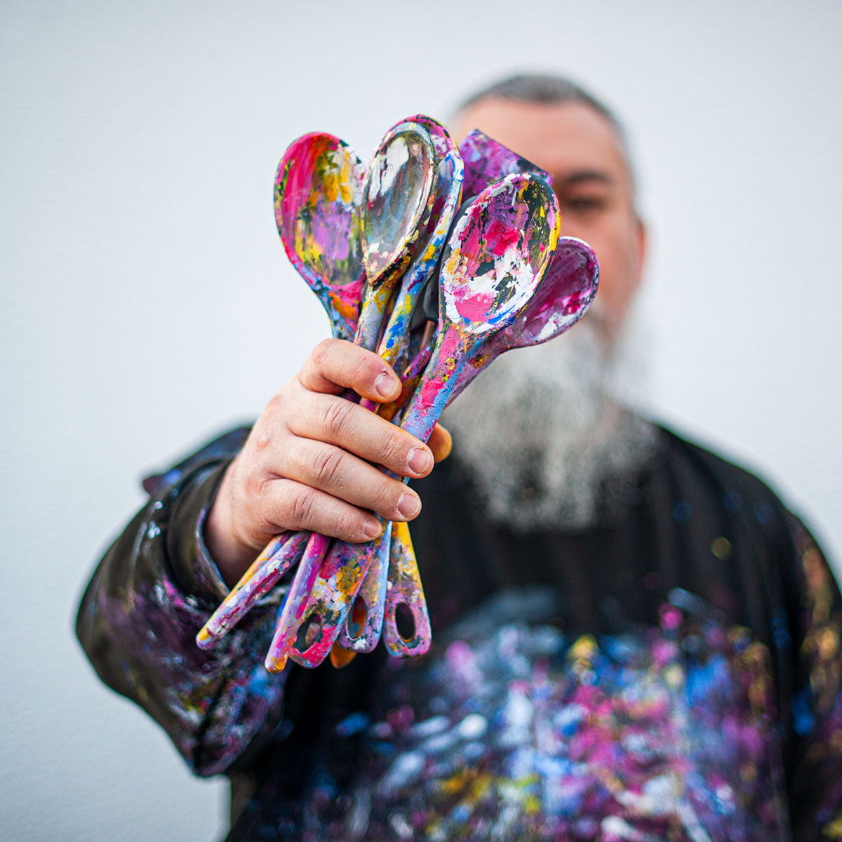 Artist holding colourful paint tools covered in layers of paint, representing texture and expression.