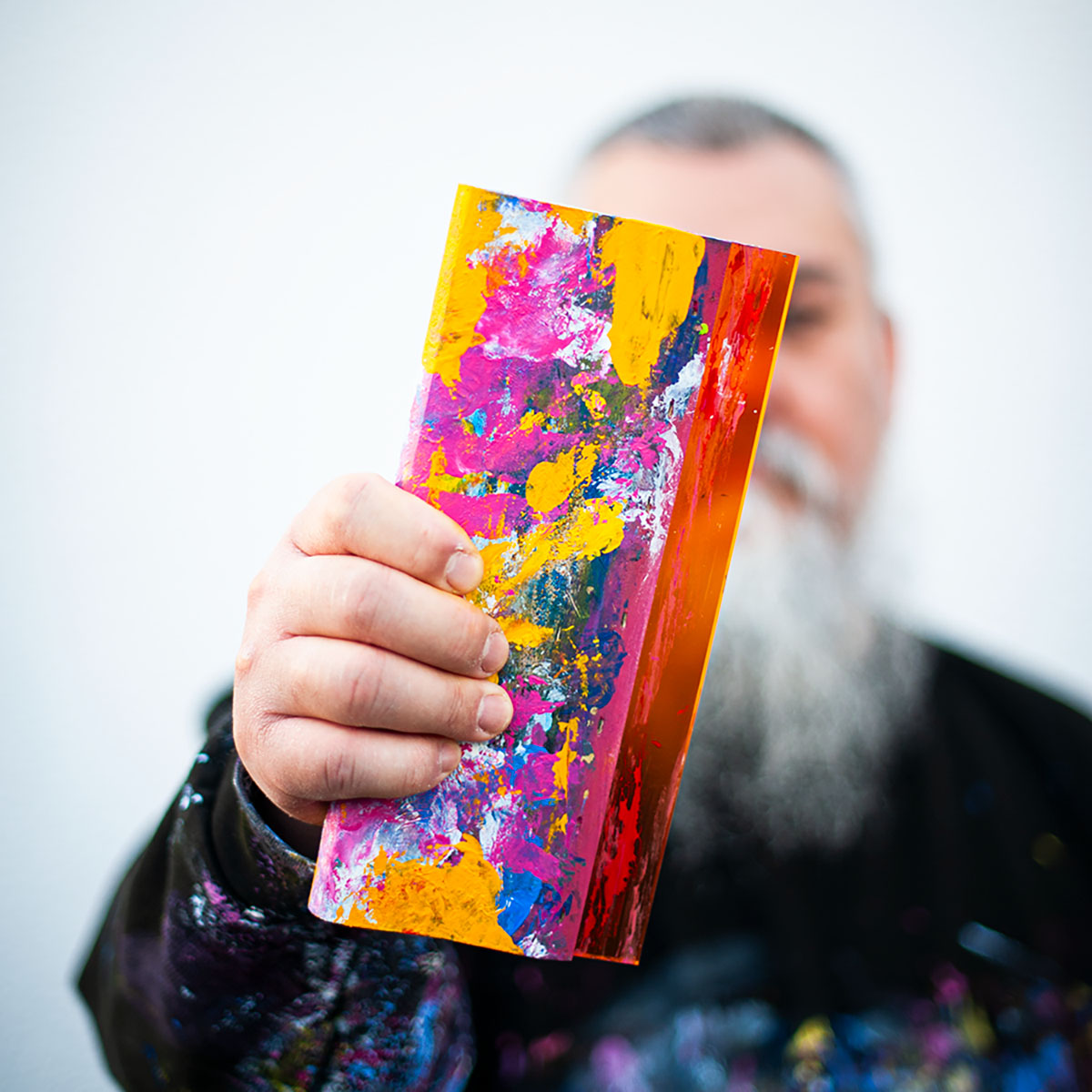 Abstract painter holding a small, colourful acrylic artwork on aluminium